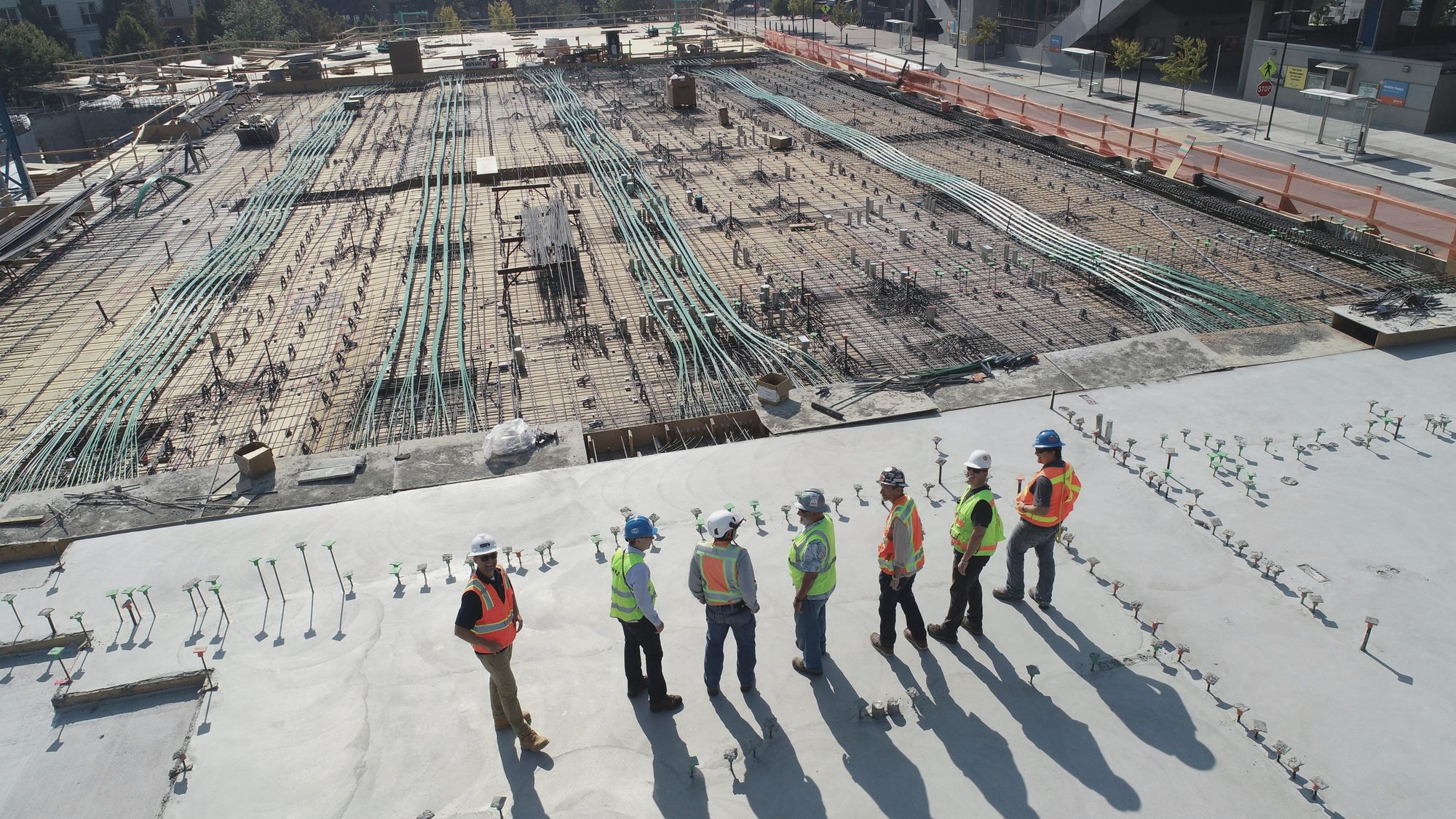 Seven workers in hard hats and hi-vis vests on a concrete deck, each outlined by an AI detection box