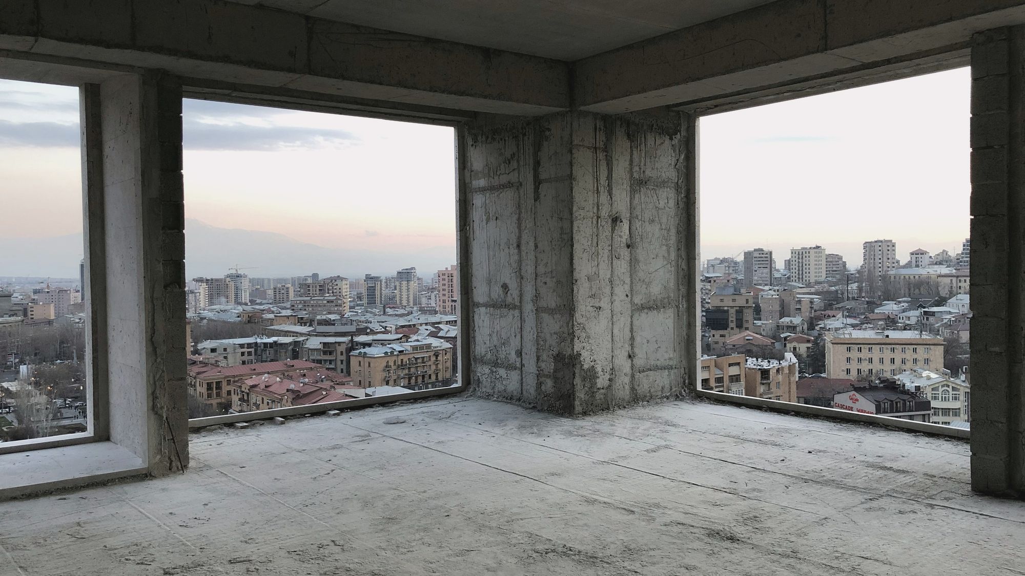 A bare concrete apartment shell with two large window openings looking out over a city
