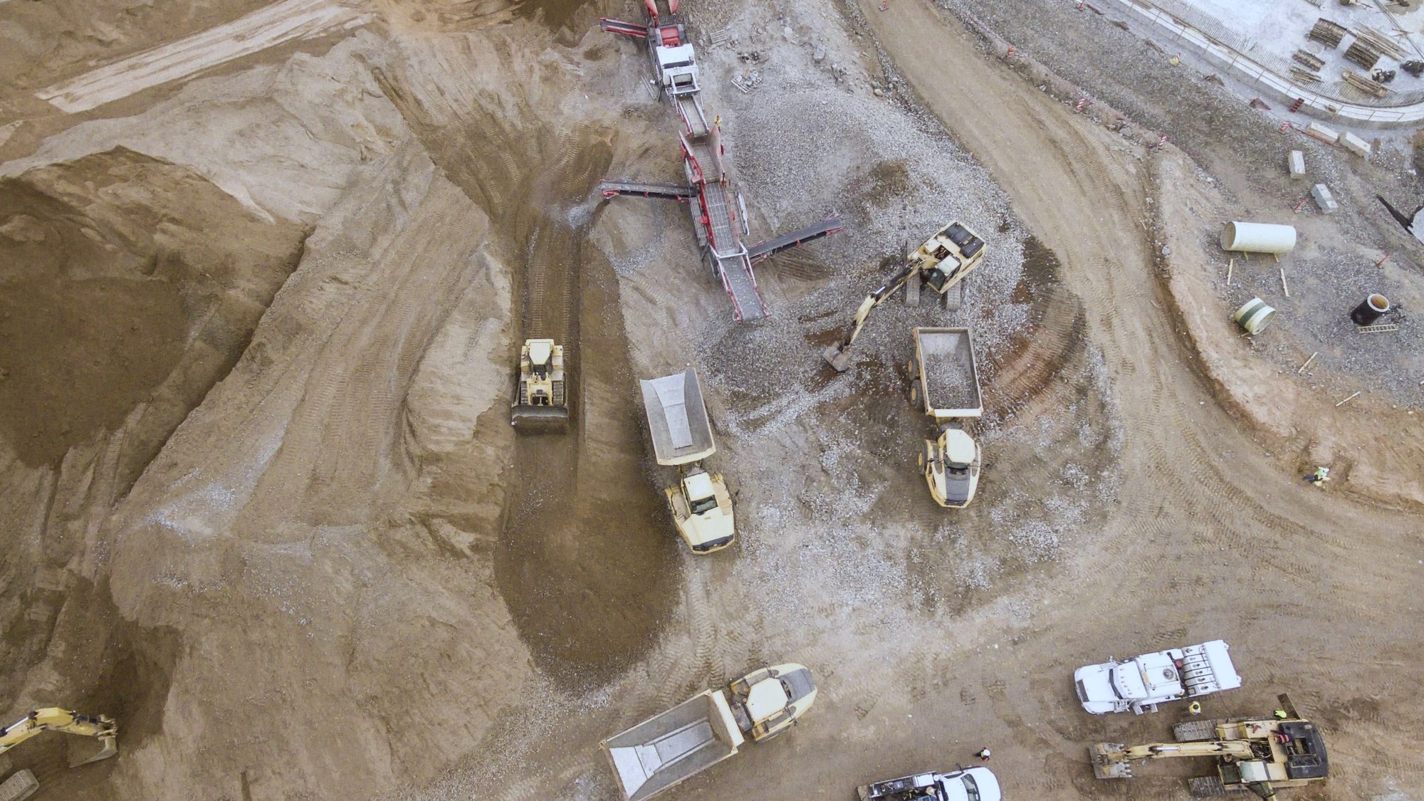Drone view straight down onto an earthworks site, with dump trucks and excavators moving soil