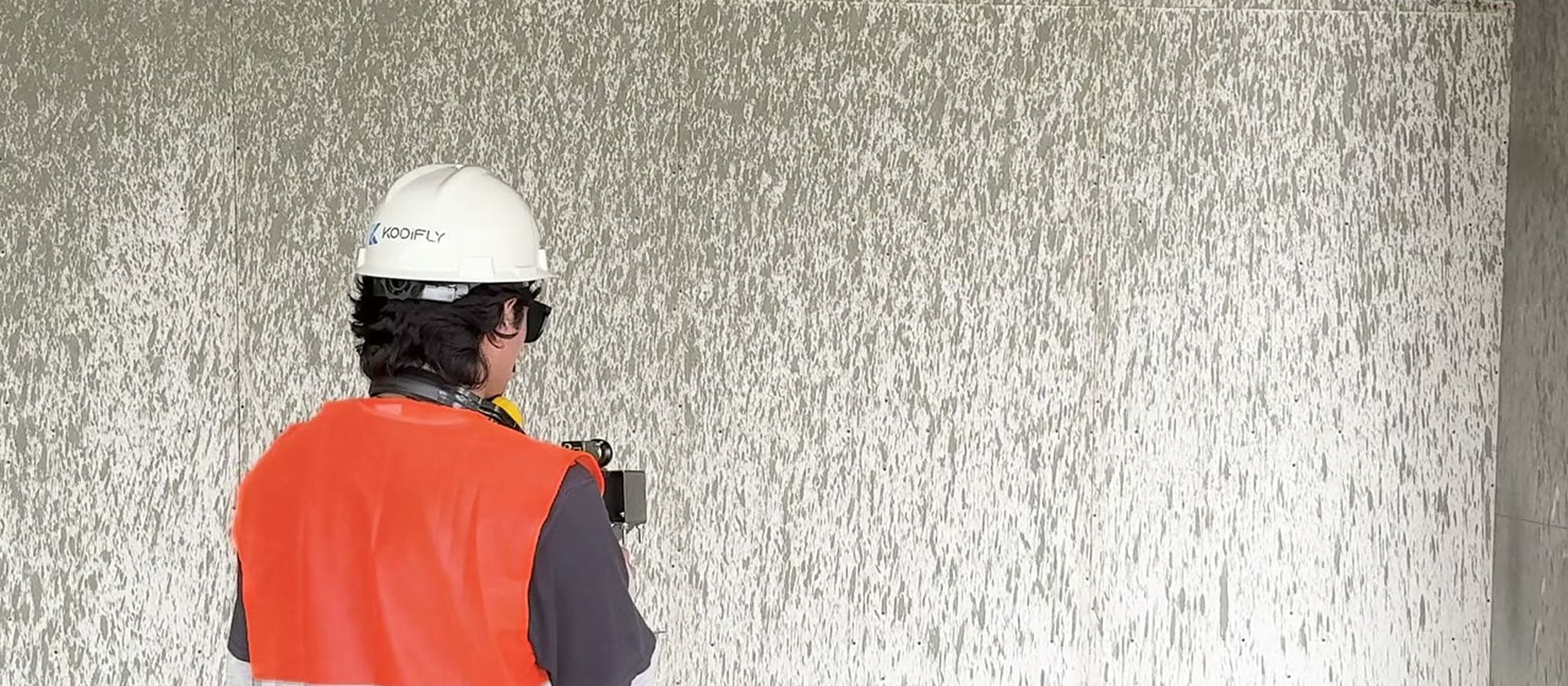Site engineer in a hard hat and hi-vis vest capturing a building floor with a handheld scanner