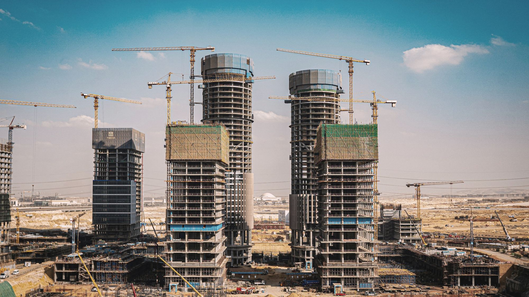High-rise towers under construction among tower cranes on a desert site